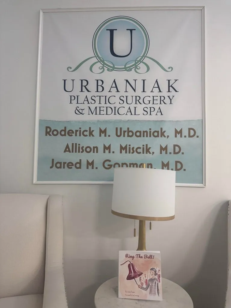 A copy of Ring the Bell! on a side table beneath the Urbaniak Plastic Surgery and Medical Spa sign